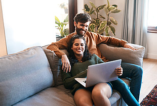 Junges Paar sitzt am Laptop auf dem Sofa