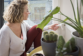 Thermostat einstellen: Eine Frau stellt das Heizungsthermostat am Hezkörper ein.